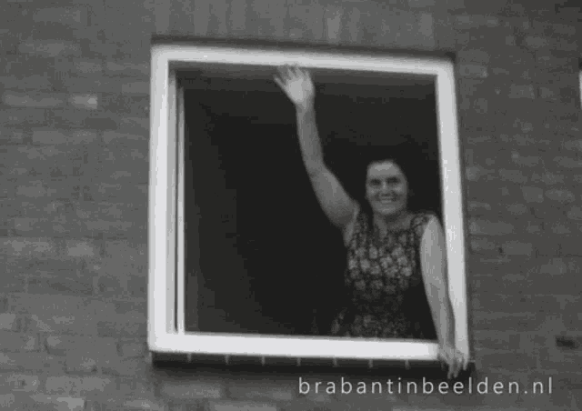 a black and white photo of a woman waving from a window with brabantinbeelden.nl written below it