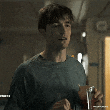 a man in a grey shirt is holding a glass with a straw in his hand .