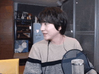 a man wearing a sweater and headphones stands in front of a microphone in a room