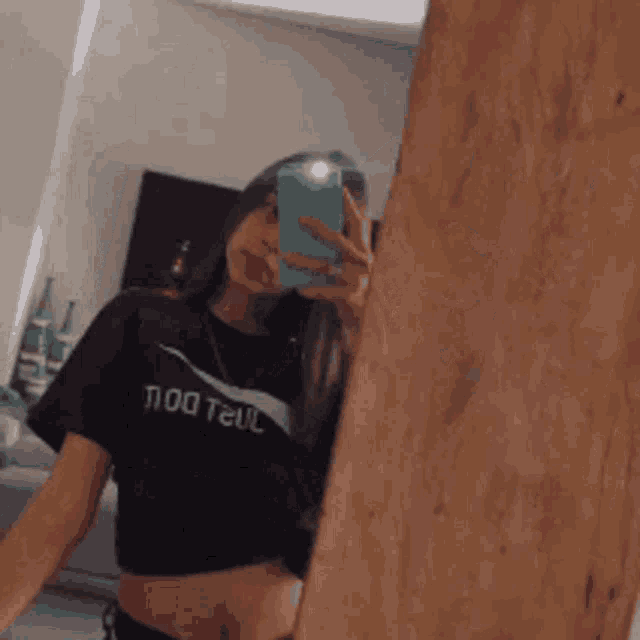 a girl is taking a selfie in front of a mirror while wearing a crop top and a nike shirt .