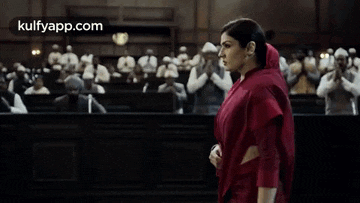 a woman in a red dress is walking in front of a crowd of people .