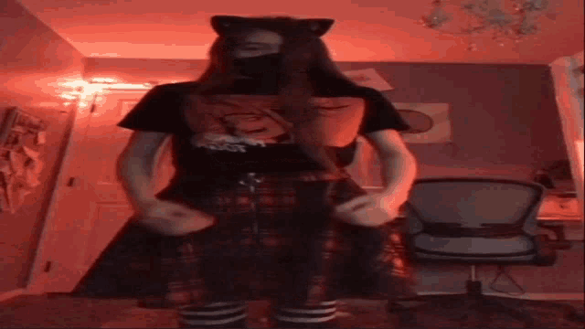 a girl wearing a black shirt and a plaid skirt is standing in a room with a chair .