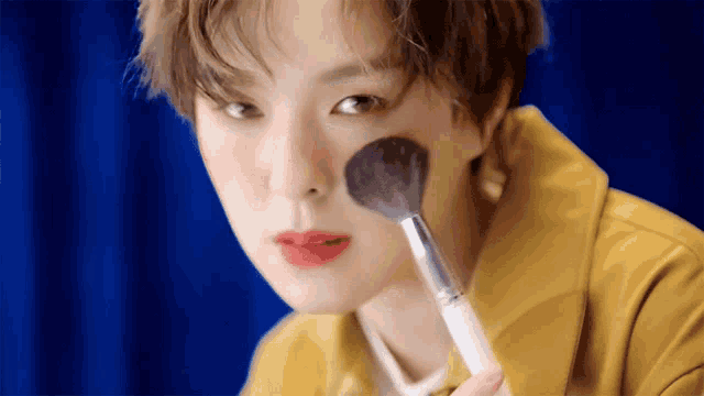 a woman in a yellow jacket is applying makeup to her face