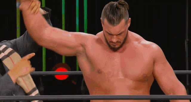 a shirtless wrestler stands in a ring with his arm raised in the air