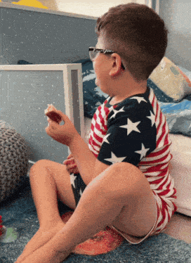 a young boy wearing glasses sits on the floor eating