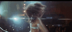 a woman is dancing on a stage with her hair blowing in the wind .