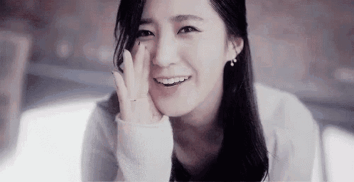 a woman is smiling with her hand on her face while sitting down .