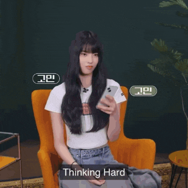 a girl is sitting in an orange chair holding a cell phone and the words thinking hard are above her head