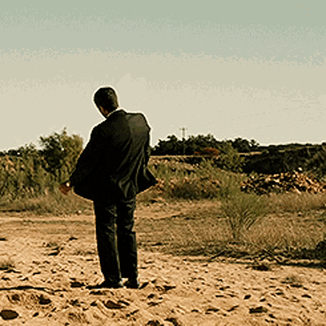 a man in a suit is standing in the middle of a dirt field