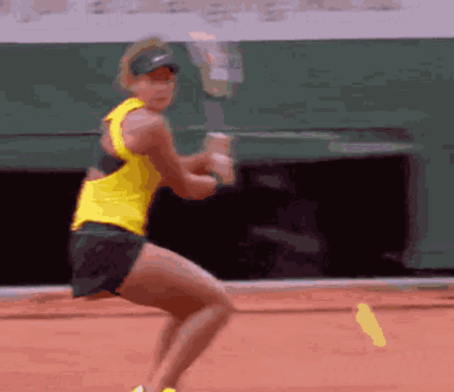 a woman in a yellow shirt is swinging a tennis racquet