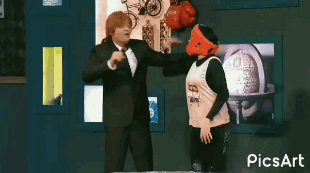 a man in a suit is talking into a microphone while a woman wearing a boxing helmet is dancing