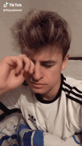 a young man in a white adidas shirt is rubbing his eye
