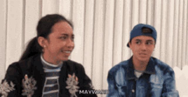 a man and a woman are sitting next to each other and the man is wearing a blue hat