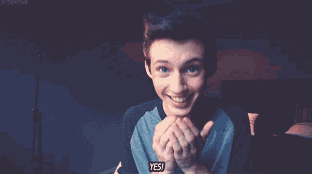 a young man is smiling and holding his hands in front of his face with the words yes written below him
