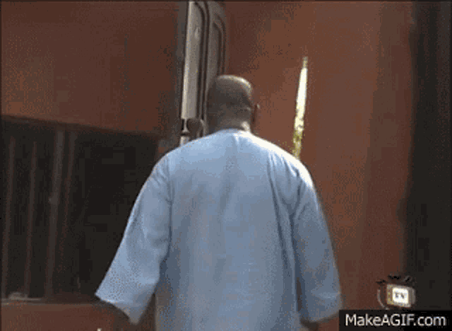 a man in a blue shirt is walking towards a door .