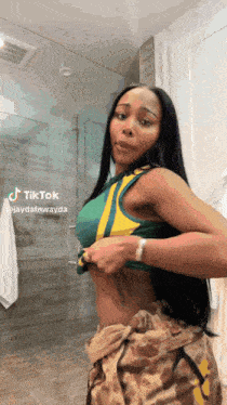 a woman in a green tank top and camo pants is standing in front of a glass shower door .