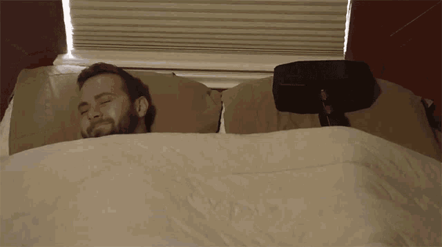 a man laying in bed with his eyes closed and a remote control on his head
