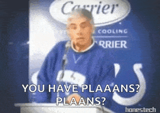 a man in a blue sweater is giving a speech in front of a carrier sign .