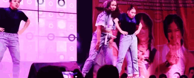 a group of people are dancing on a stage in front of a large screen with a picture of a woman on it .