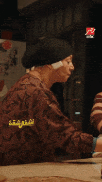 a woman sitting at a table with a mbc logo on the bottom