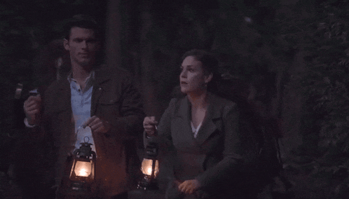 a man and a woman are walking through a dark forest holding lanterns