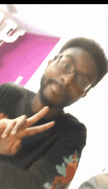 a man wearing glasses and a black shirt with roses on the sleeves is making a peace sign