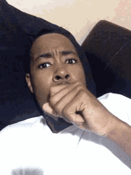 a man covering his mouth with his hand while laying on a bed