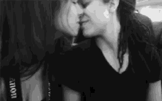 a black and white photo of two women kissing each other .
