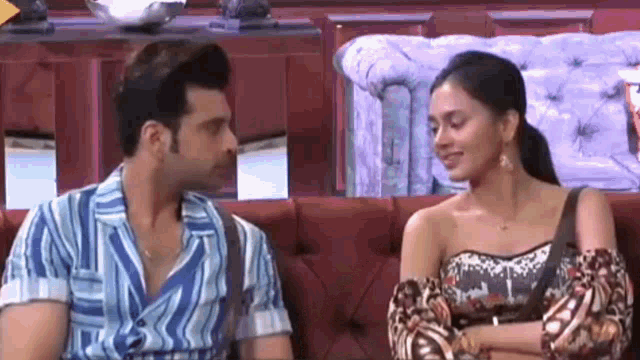 a man and a woman are sitting on a red couch looking at each other .