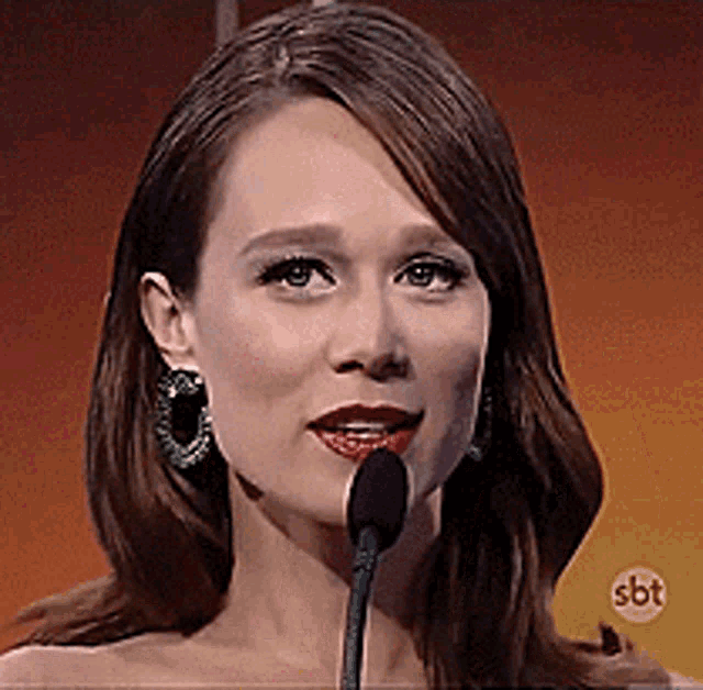 a woman is speaking into a microphone with a sbt logo in the corner