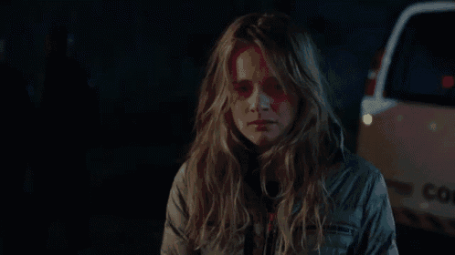 a woman with long hair is standing in front of a car at night .