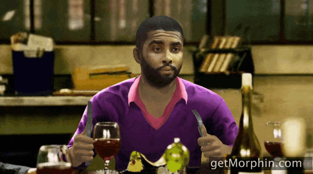 a man in a purple shirt is sitting at a table with a glass of wine and a knife and fork