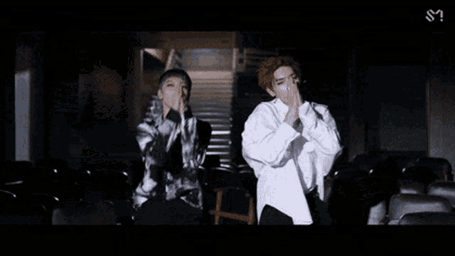 two men are dancing in a dark room with their hands on their faces .