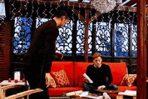 a man standing next to a man sitting on a couch