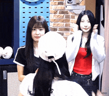 a girl in a red tank top is standing next to a girl in a white cardigan