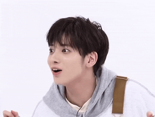 a young man wearing a gray hoodie and overalls is making a surprised face .