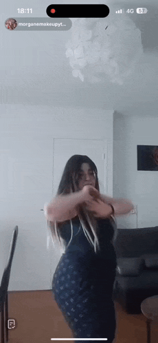 a woman in a black dress is dancing in a living room with the time of 18:11