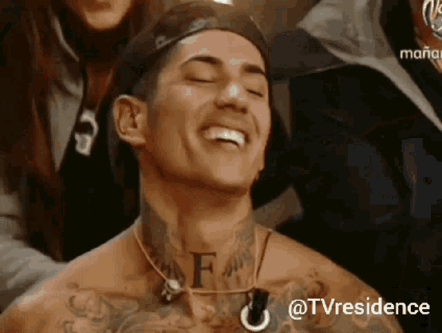 a shirtless man with a tattoo on his neck is smiling with his eyes closed .