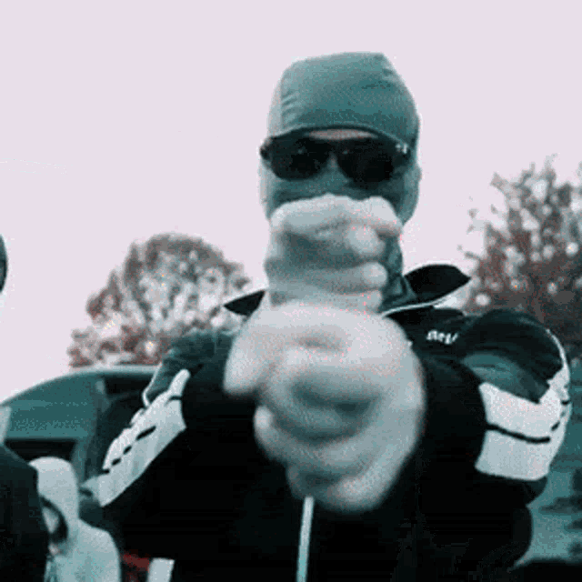 a man wearing sunglasses and a beanie is pointing at the camera