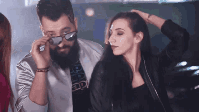 a man with a beard is adjusting his glasses while a woman holds her hair