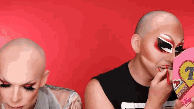 two drag queens are looking at their faces in a mirror with a heart on it