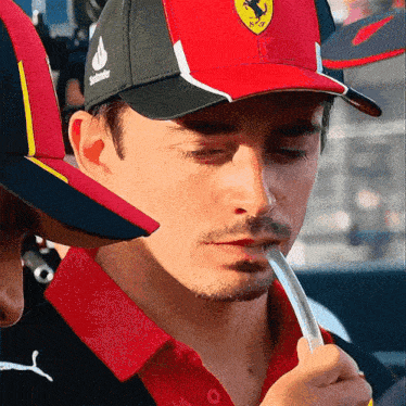 a man wearing a red and black ferrari hat holds a straw in his mouth