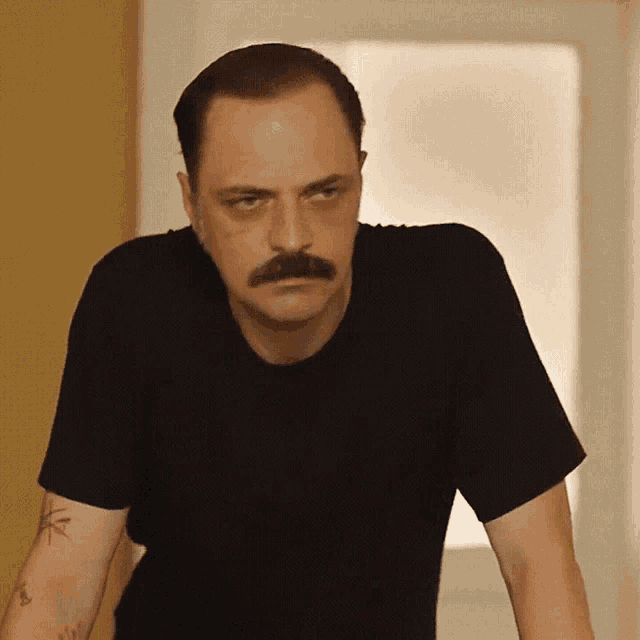 a man with a mustache wearing a black shirt has a tattoo on his arm