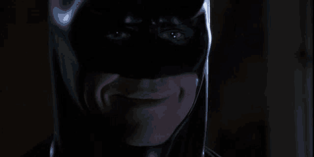 a close up of a man wearing a batman mask smiling .