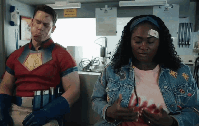 a man in a superhero costume is sitting next to a woman with a bandage on her forehead