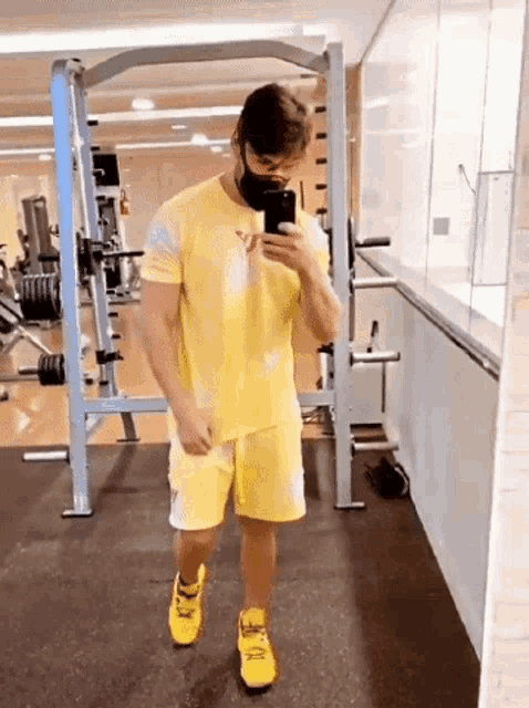 a man in a yellow shirt and yellow shorts is taking a picture of himself in a gym .