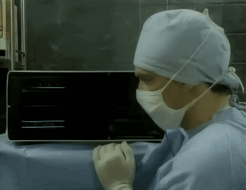 a surgeon wearing a mask and gloves is looking at a monitor