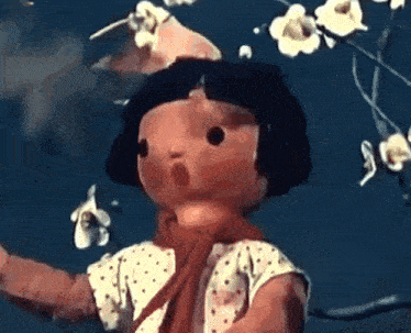 a doll is standing in front of a tree with flowers on it 's head .