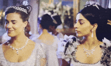 two women wearing tiaras and necklaces are standing next to each other in a room .
