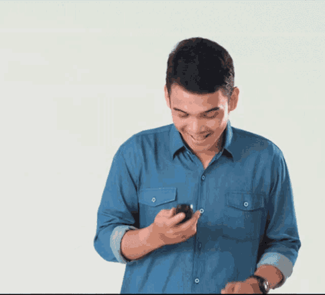 a man in a blue shirt is holding a cell phone and smiling